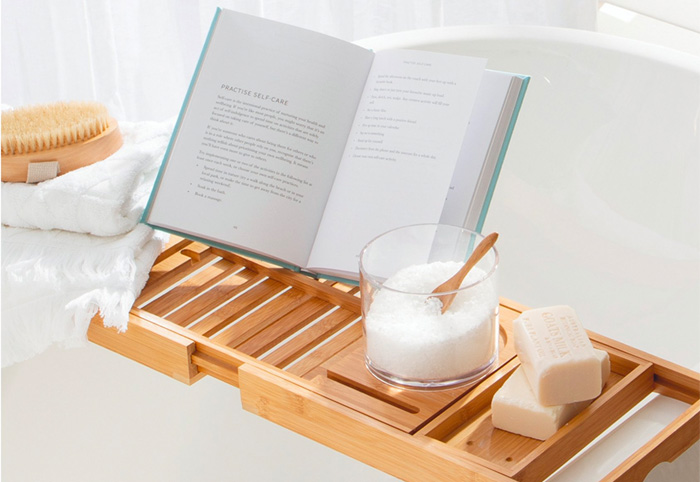Natural wood bath caddy holding a book and soap.