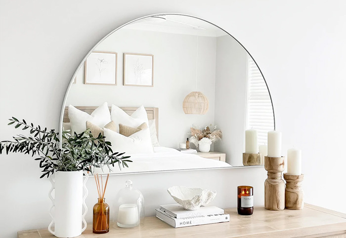 Wall-mounted white arched mirror above a chest of wooden drawers. 