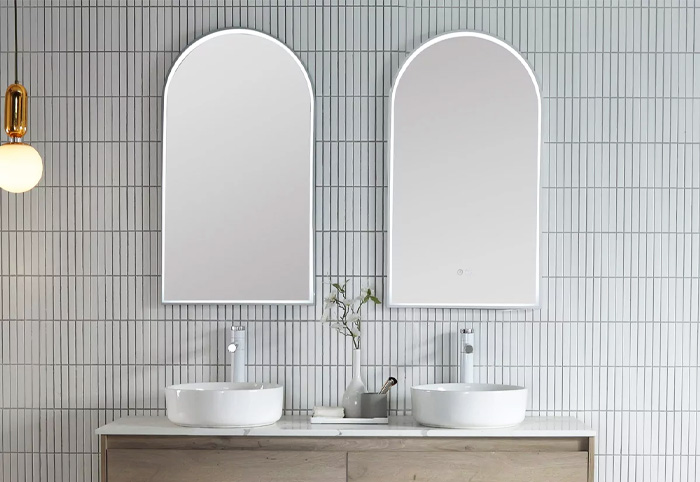 LED arched bathroom mirrors mounted against a tiled wall above a double vanity.
