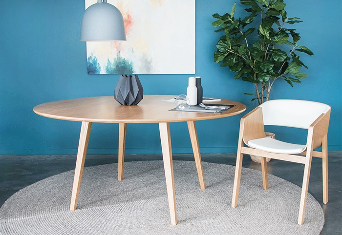 Round oak dining table with matching chair against a bright blue wall.