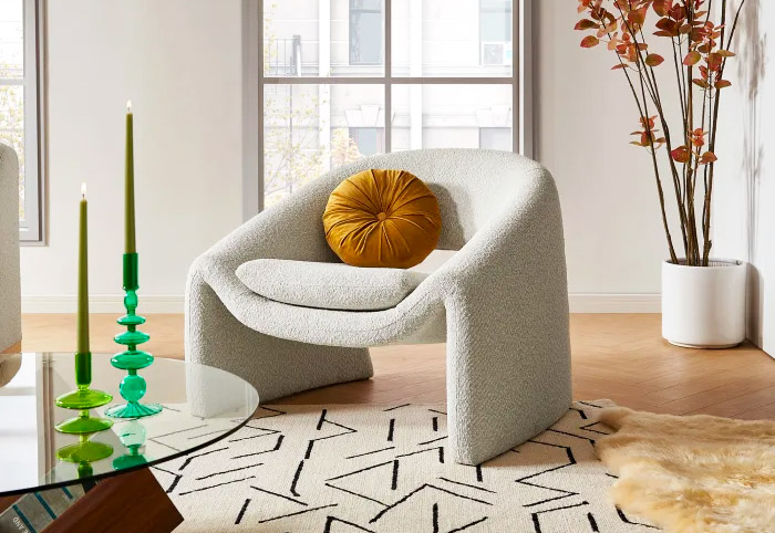 Unique white boucle armchair pictured in a patterned rug and tan throw cushion.