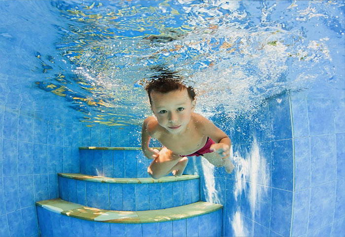 Boy in red bathers swimming underwater without goggles.