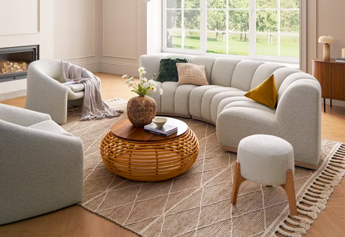 Curved beige sofa in a living room next to armchairs.