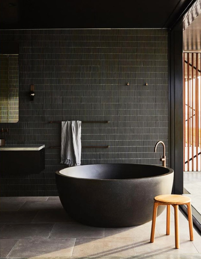 A circular black stone bath tub in a contemporary bathroom.
