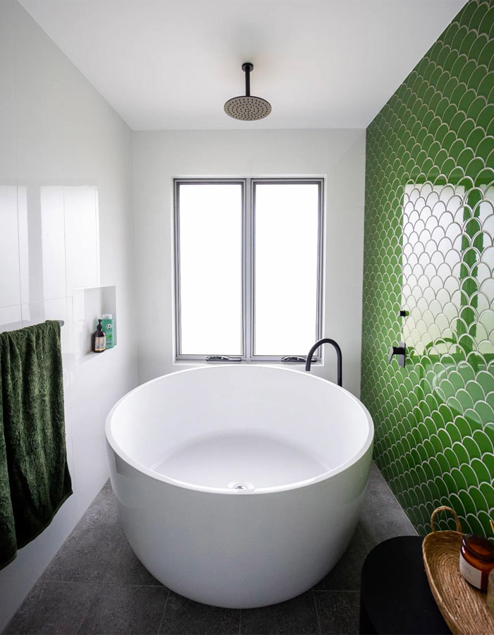 White circular bath tub against a green tiled wall.
