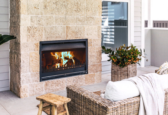 Outdoor fireplace mounted into a stone wall opposite a sofa.