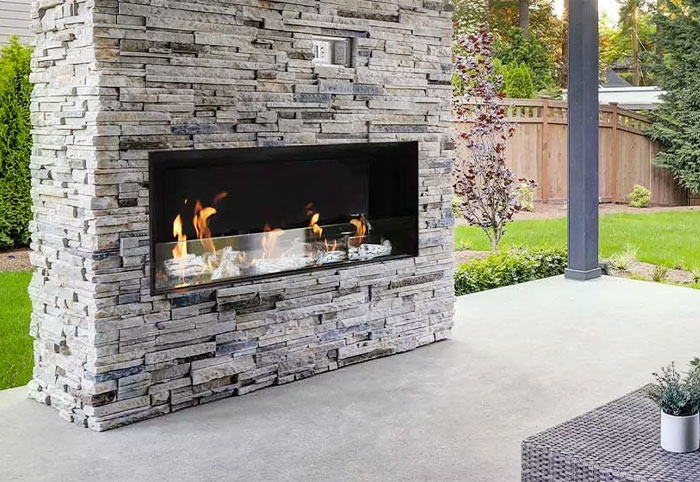 An outdoor gas fireplace built into a stone column.