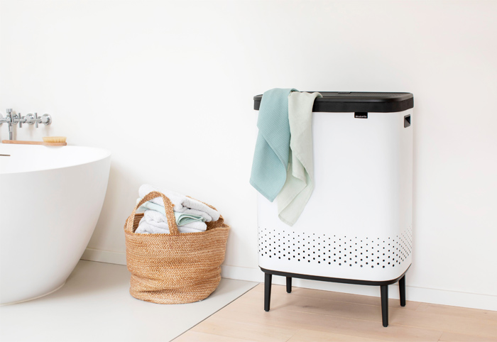 White laundry bin containing towels positioned next to bath tub.