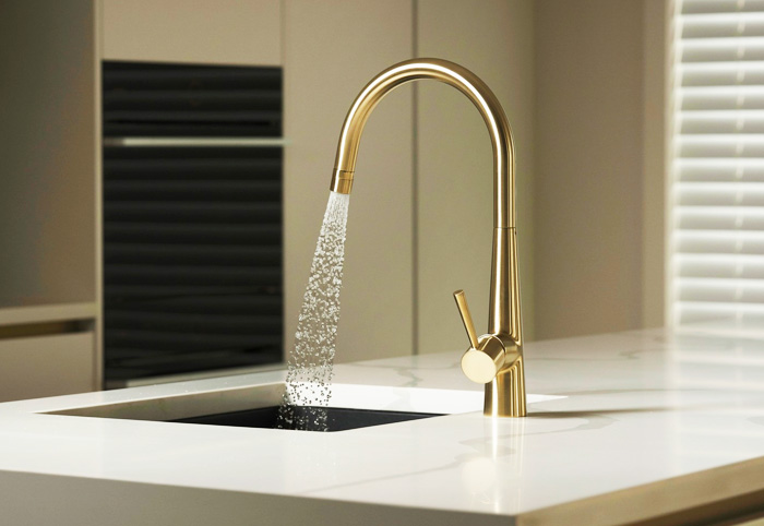 Water sprays from a brushed brass kitchen mixer.