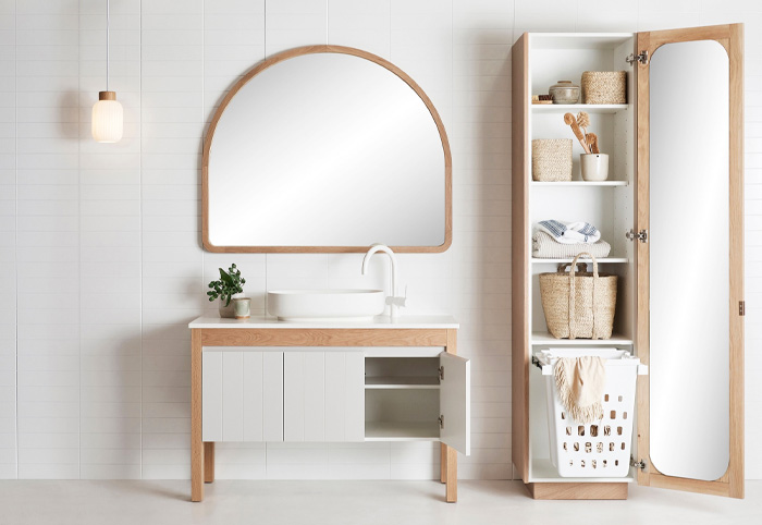 A curved wooden mirror sits above a small bathroom vanity with a white sink and tap.
