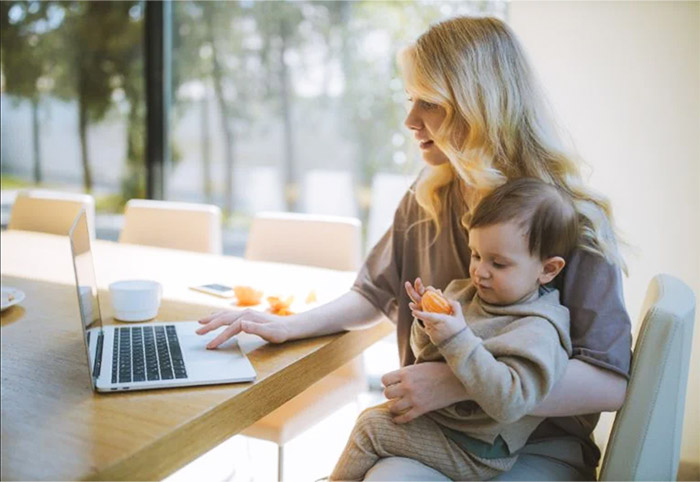 Woman works at a laptop with a child on her lap.