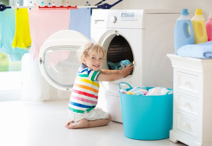 Smiling boy puts clothes into a front-loader washing machine.