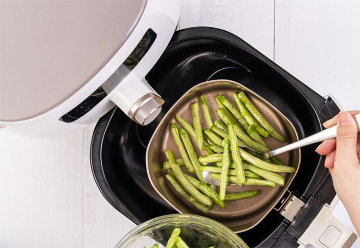 Steamed green beans being lifted from an airfryer.