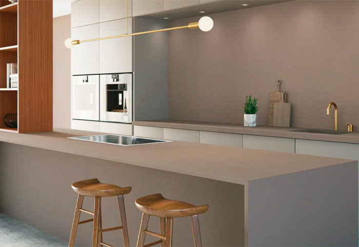 Warm-grey minimalist kitchen with gold tapware and wooden stools.