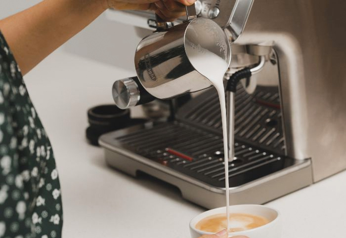 Woman using the De'Longhi La Specialista Arte Evo Coffee machine pours milk into a mug.