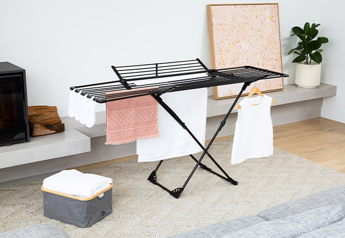 Black winged clothes airer in a living room next to a hamper.