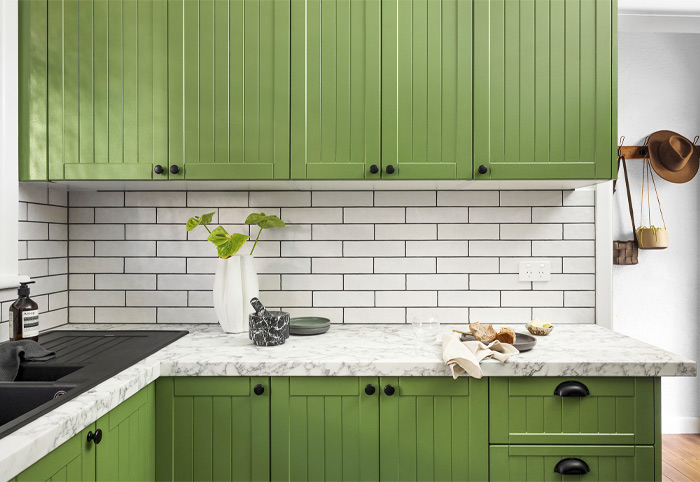 Green kitchen cabinets with black knob handles.