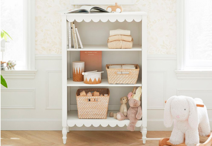 White bookcase with petal trim next to a nursing chair in a child's room.