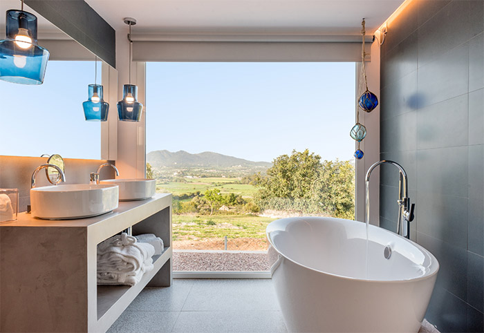 Freestanding bath next to an oversized window looking out onto the countryside.