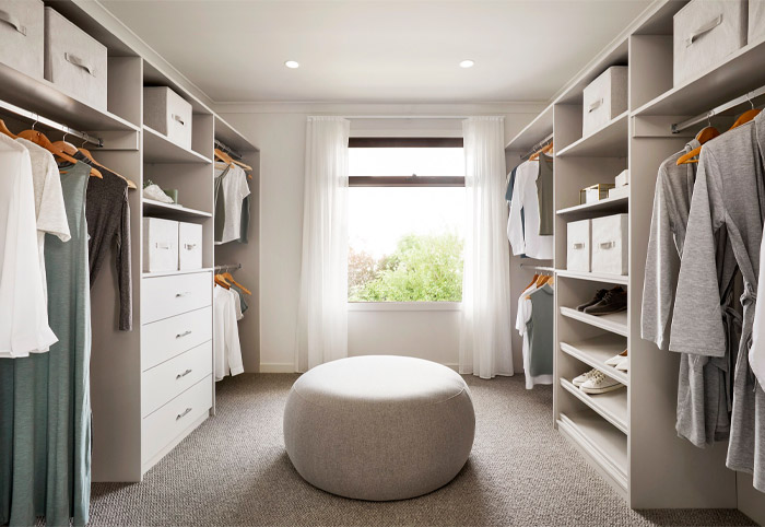 Neutral closet with large ottoman in the centre and an open window at one end.