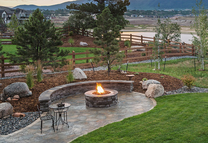 A country backyard with a stone fire pit on a paved entertaining area.