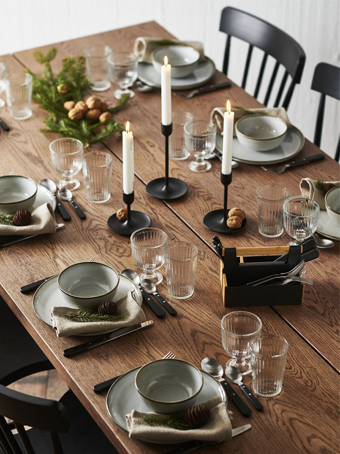 Brown wooden table set with rustic tableware and black candlesticks.