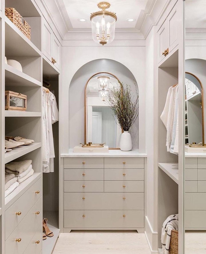 French-style walk-in closet with arched mirror at one end and gold handles throughout. 