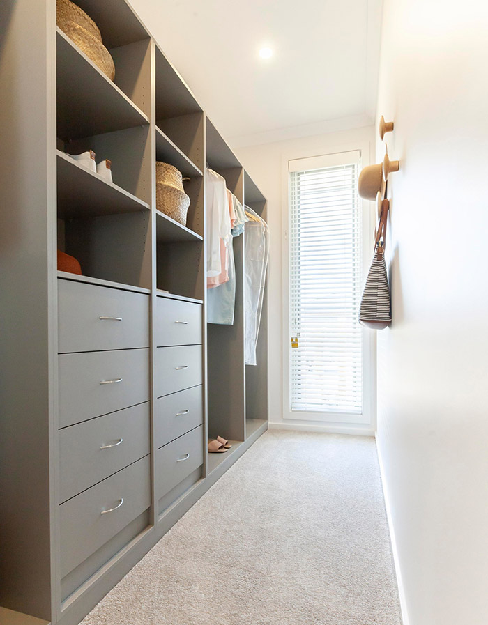 A modern closet with grey cabinetry throughout and a full-length window at the end. 