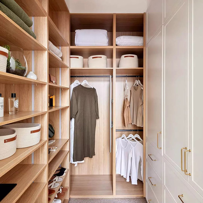 A walk-in wardrobe with loads of wooden shelving and white cabinets.