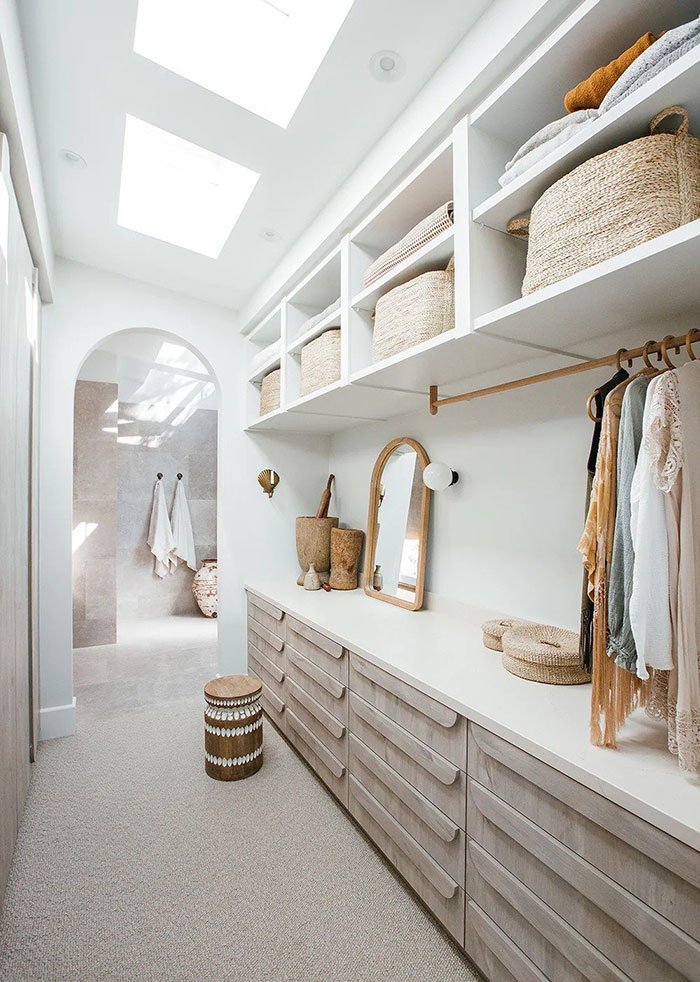 Coastal-style walk-in wardrobe with light wood drawers, an arched entry and wicker baskets throughout.