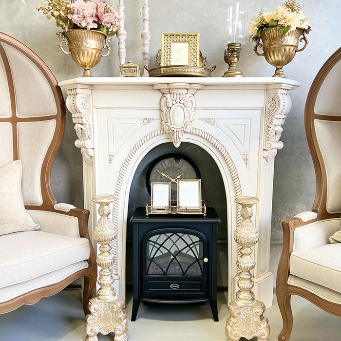 A white stone mantle with French mouldings in between two armchairs.
