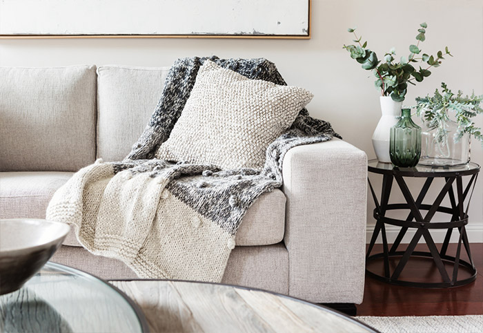Neutral sofa draped in a throw rug and decorated with a textured neutral cushion.