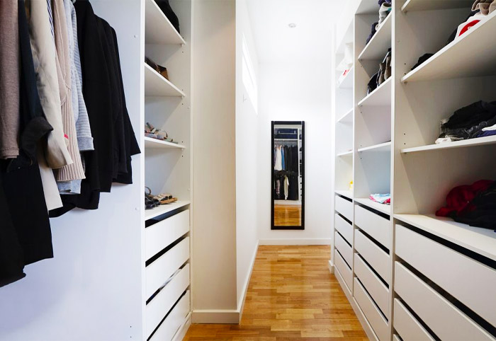 A white closet space with glossy wooden floorboards. 