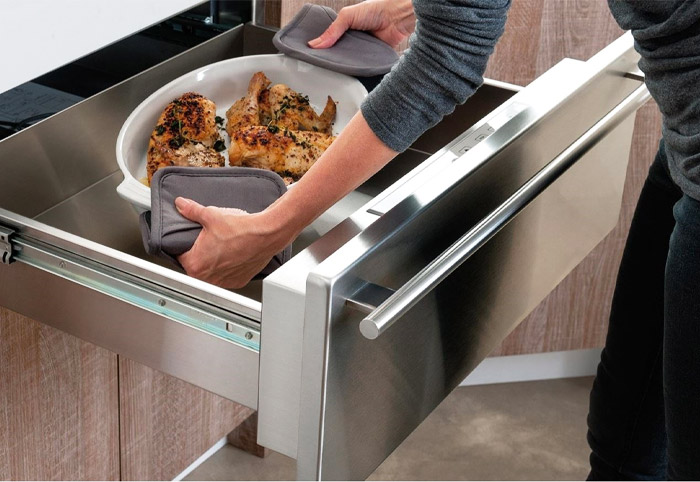 Person lifts a dish of food from a warming drawer in an outdoor kitchen.