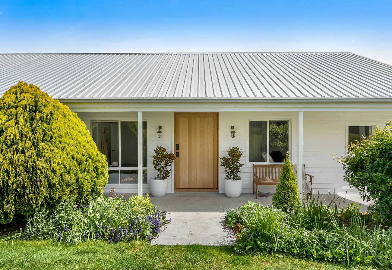 Front of a white weatherboard house with a timber door.