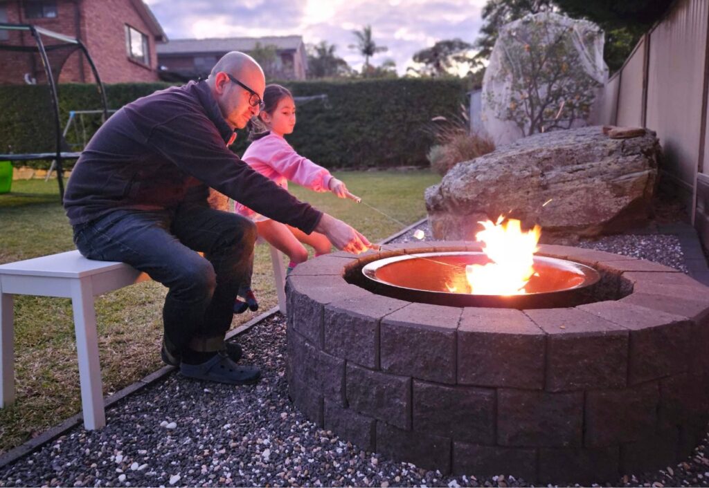 A father and child toast marshmallows at a fire pit.