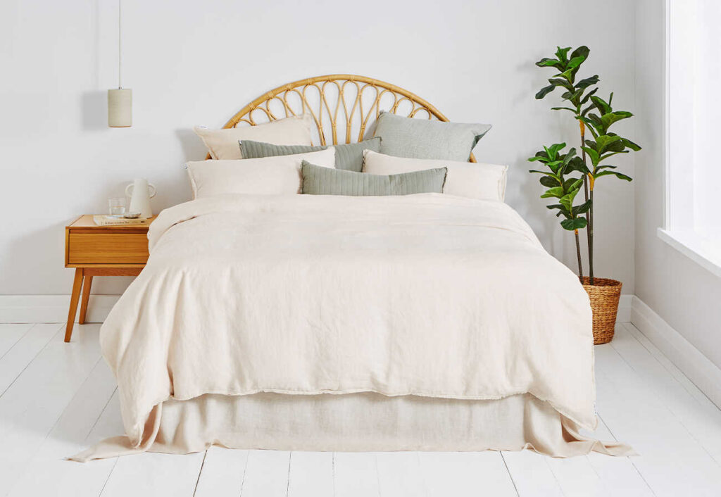 Dri-Glo natural linen quilt cover shown on a bed with a rattan bedhead.