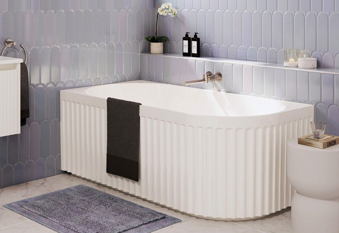 Corner freestanding bath against a blue tiled wall.