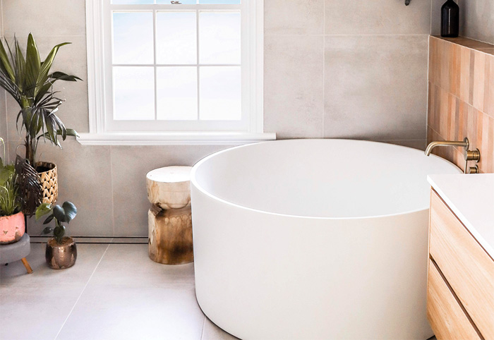 White round bathtub in the corner of a bathroom with brass tapware.