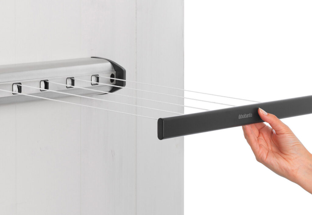 A woman's hand pulling the Brabantia extendable  clothesline from it's wall-mounted base unit.