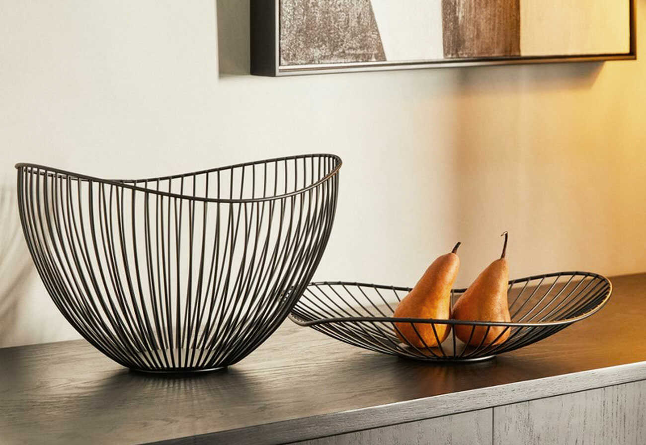 Black wire fruit bowls on top of a buffet unit. 