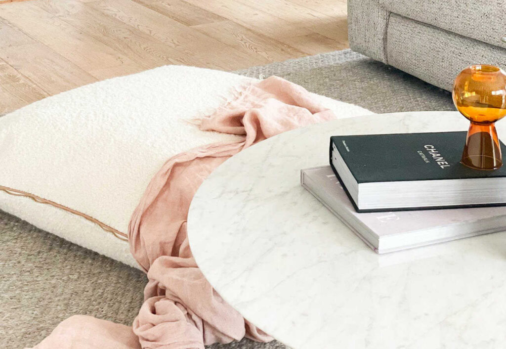 Ivory boucle floor cushion next to a marble coffee table in a living room.