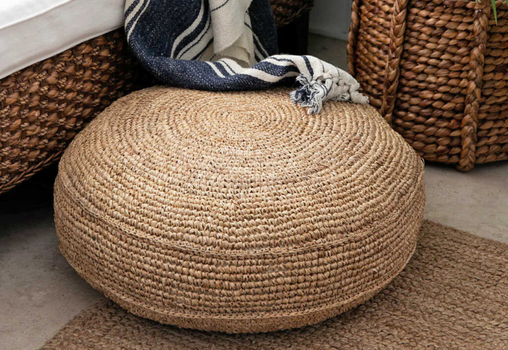 Large raffia floor cushion next to a bed.