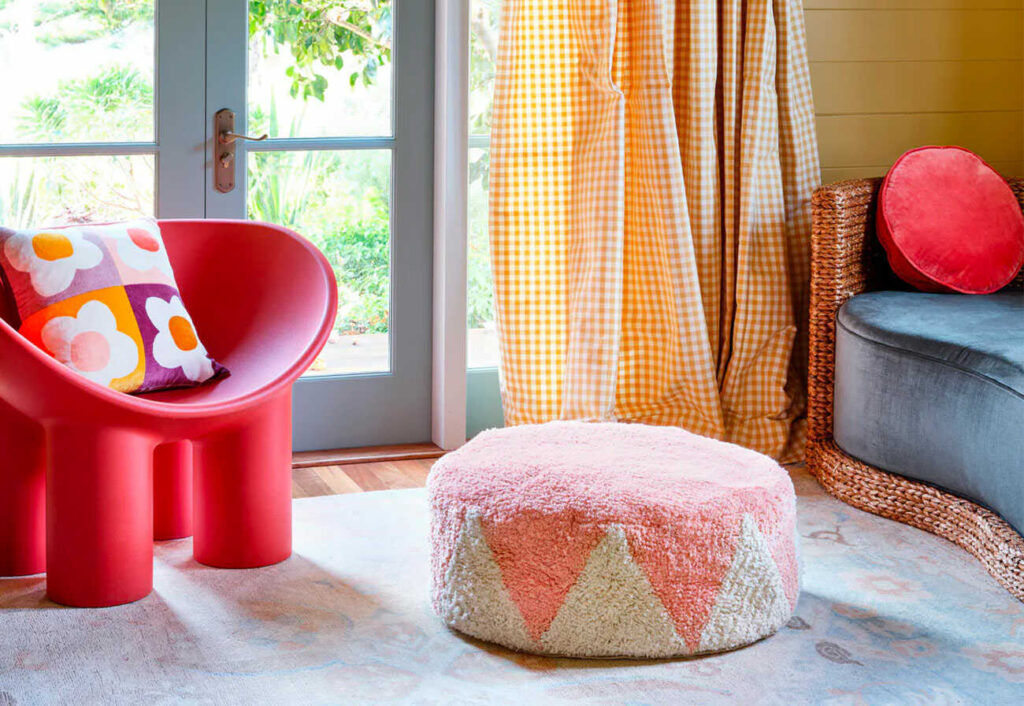 Pink and white floor cushion on a rug next to a red chair and blue sofa. 