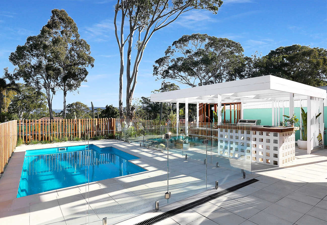 Backyard pool and pool house featuring concrete paving.