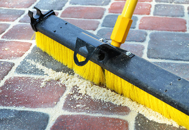 Broom sweeping sand into brick joins.
