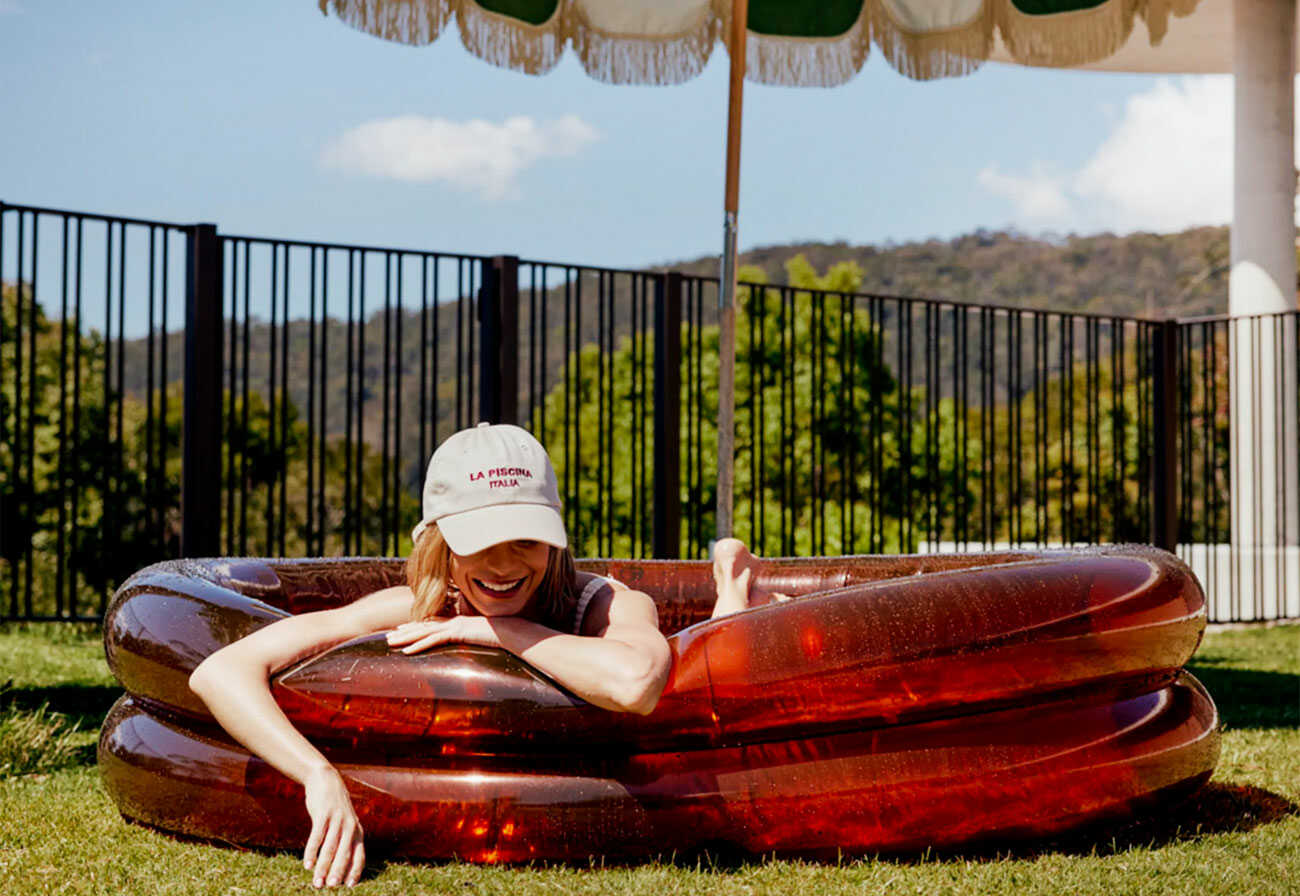 Women lying in am amber-coloured inflatable pool on a lawn. 