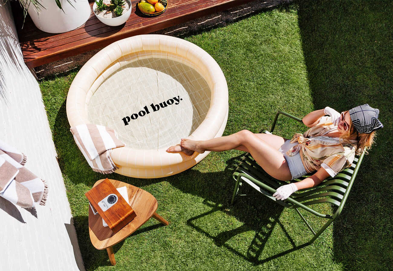 Woman sitting on a green outdoor chair next to a paddling pool.