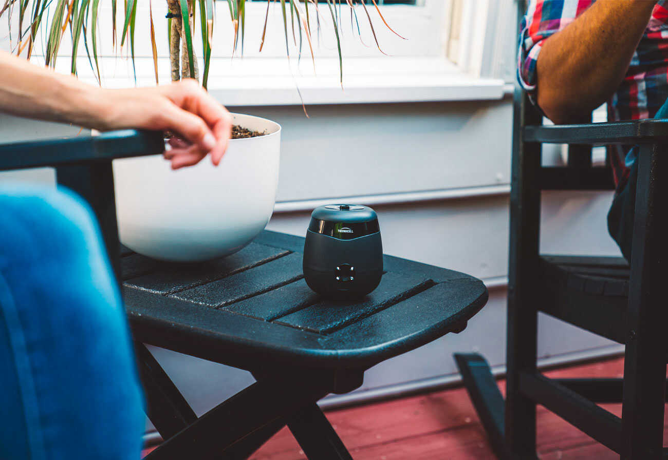 Black Thermacell Mosquito Repeller sits on a small outdoor table between two people.