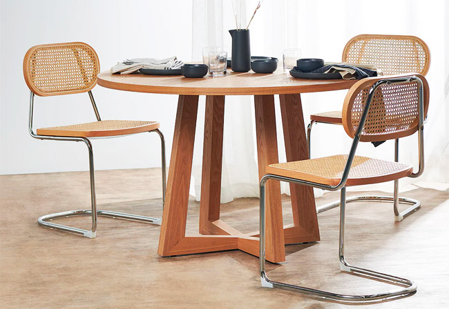 Round wooden dining table with geometric legs.